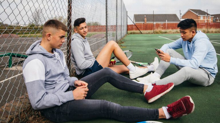 three teenage boys sit down on a tennis court
