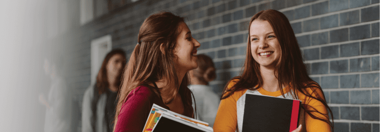two girls smiling and holding textbooks